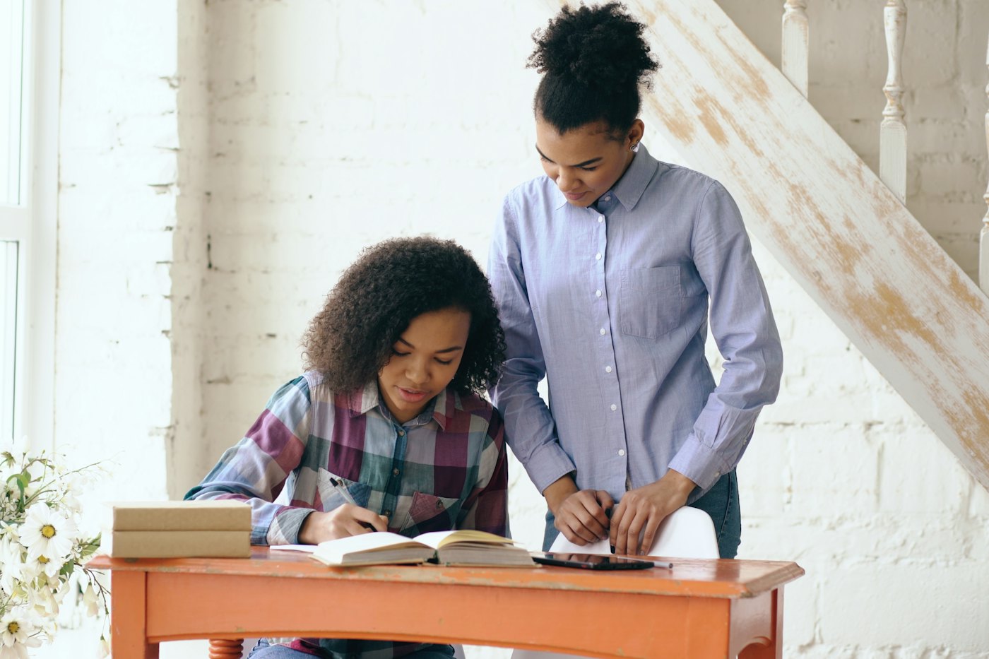 A young woman helps a teen girl with her homework at a desk