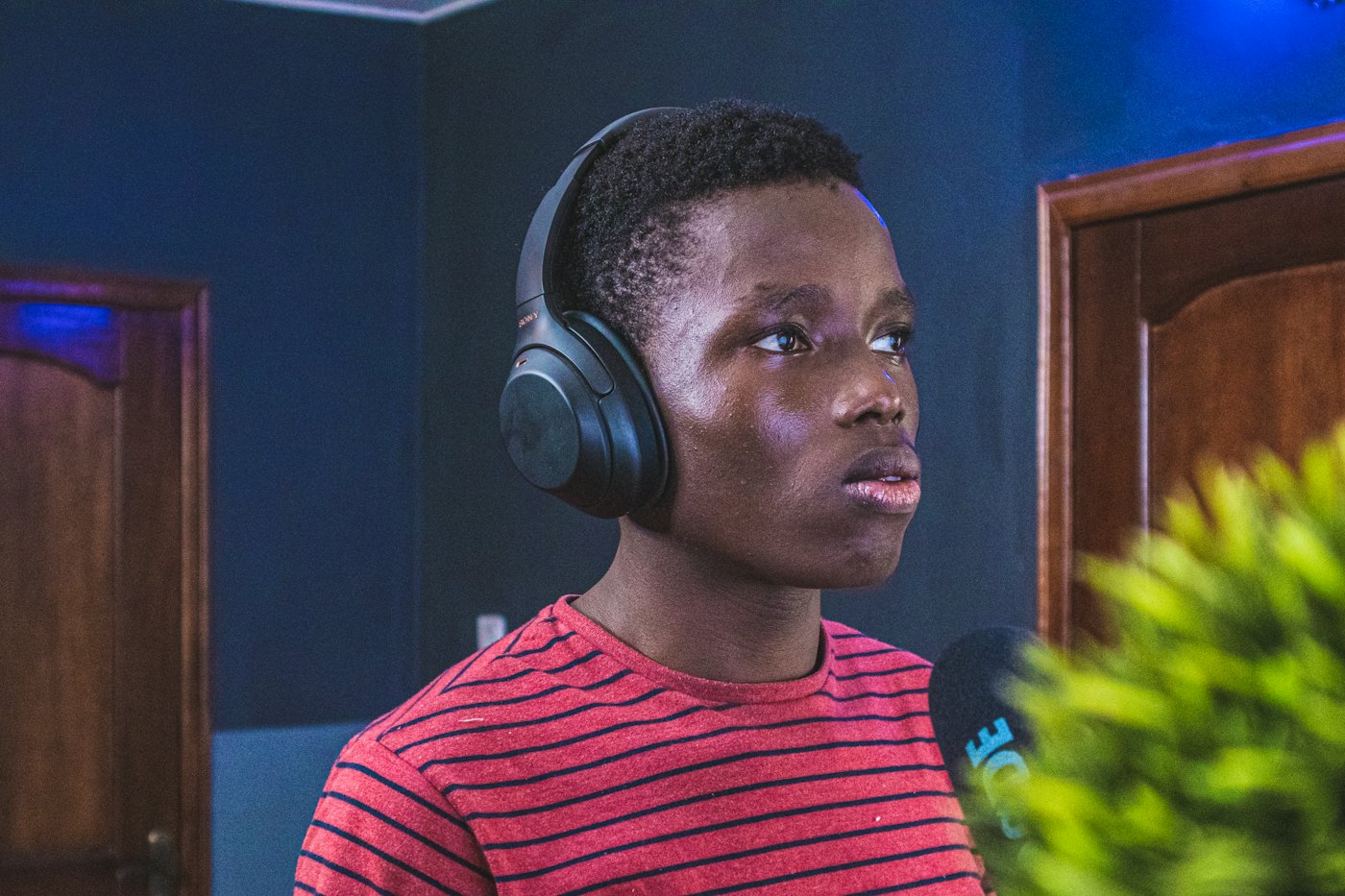 A teen wearing headphones focuses at a microphone in a recording studio
