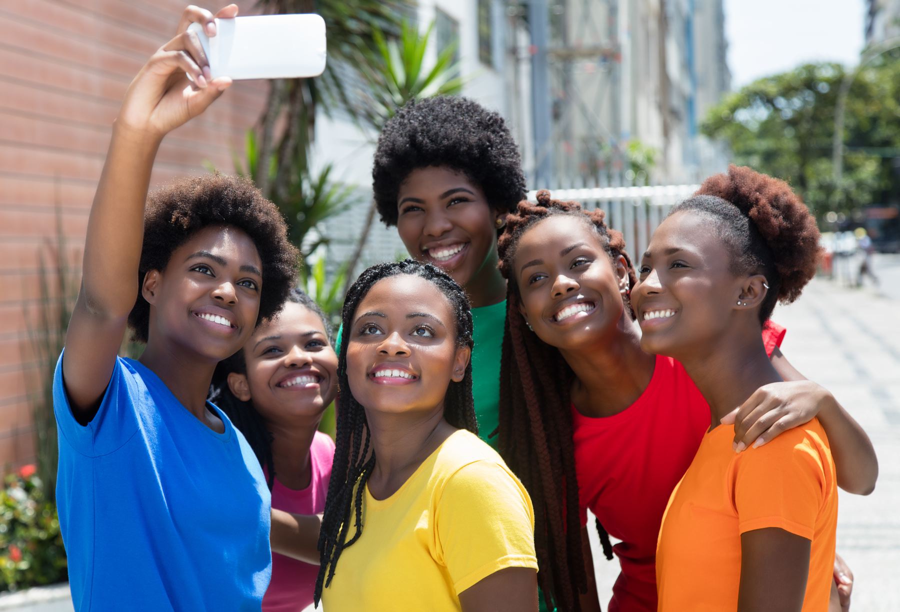Six smiling teen girls in bright T-shirts take a selfie together outdoors