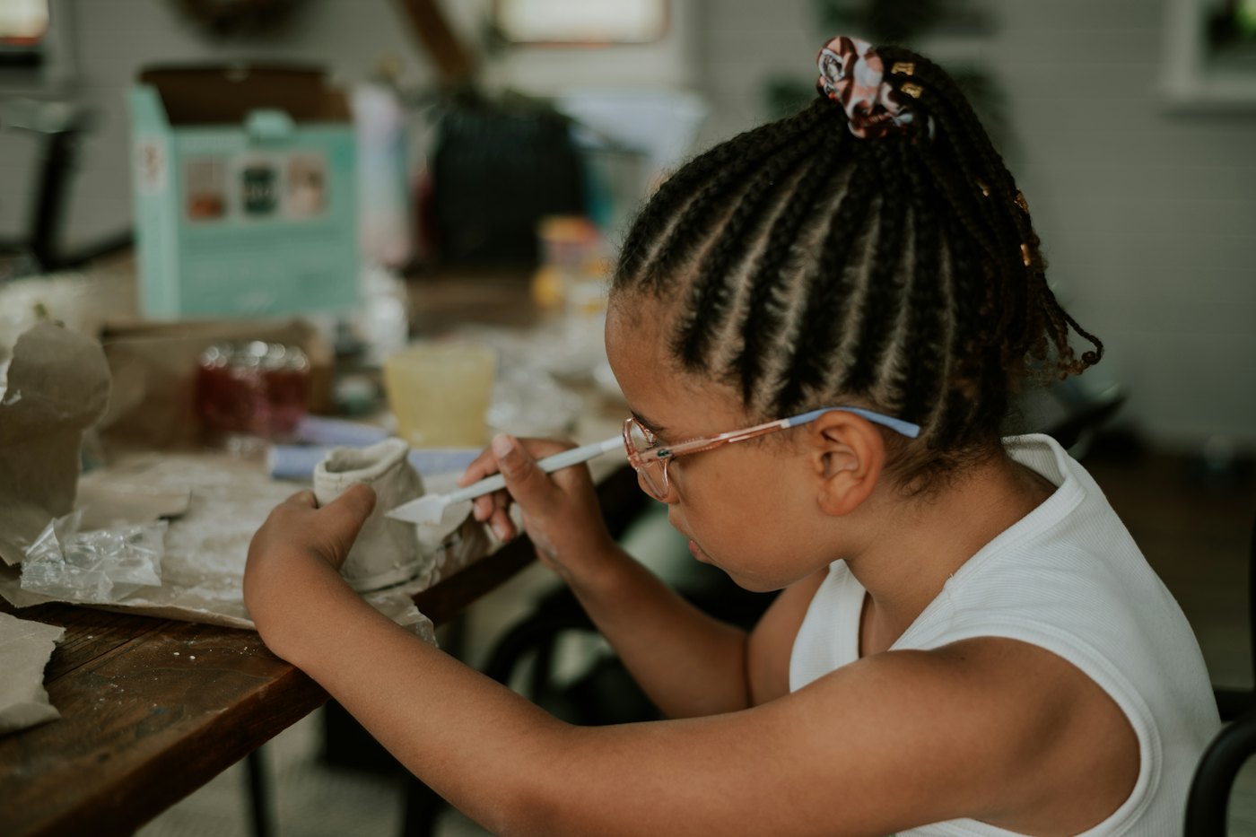 A girl in glasses shapes a clay pot at an art table