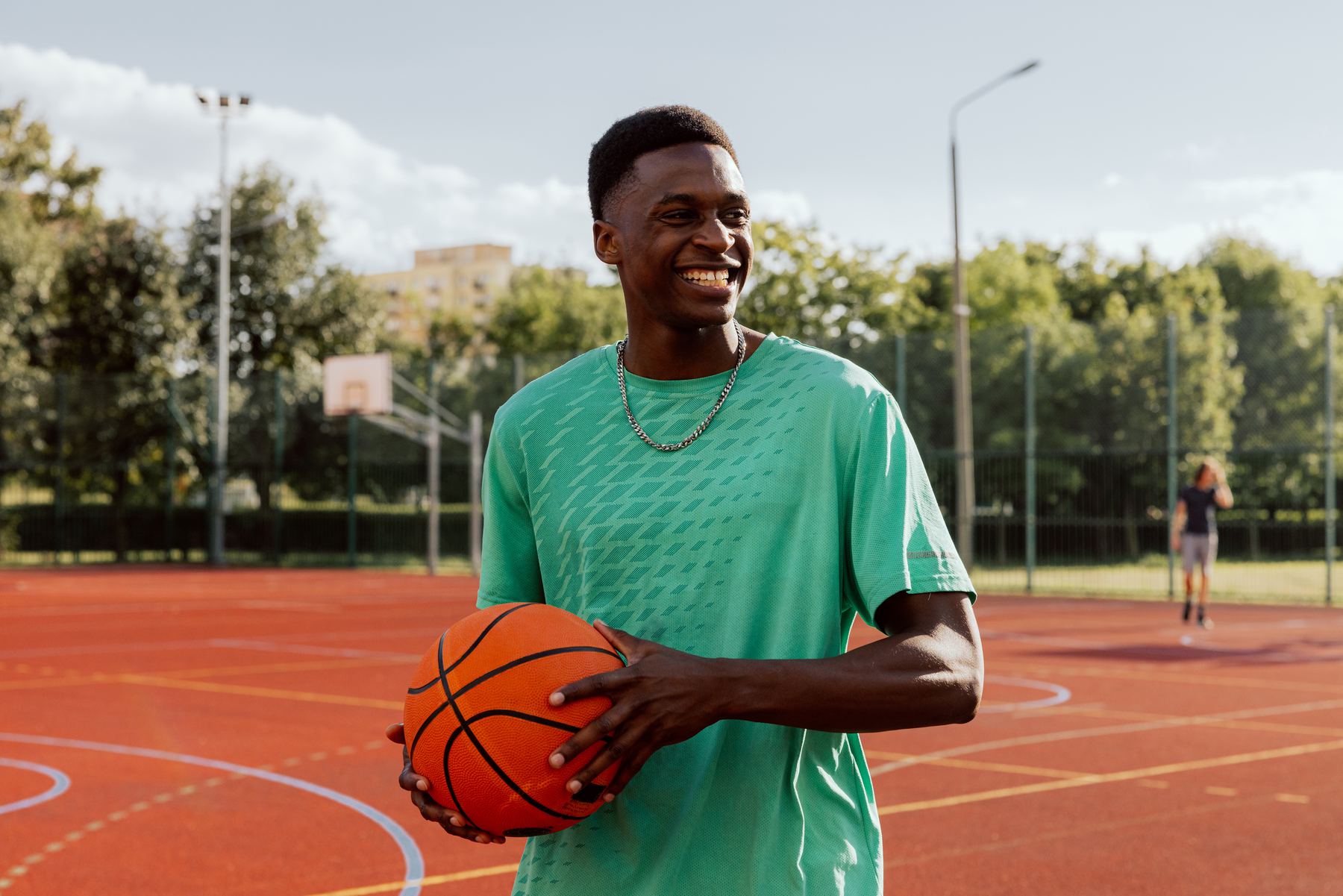 A smiling young man holds a basketball on an outdoor court