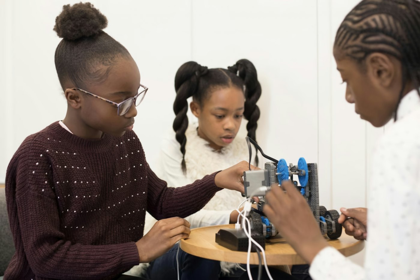 Three girls build and wire a small robot together at a table