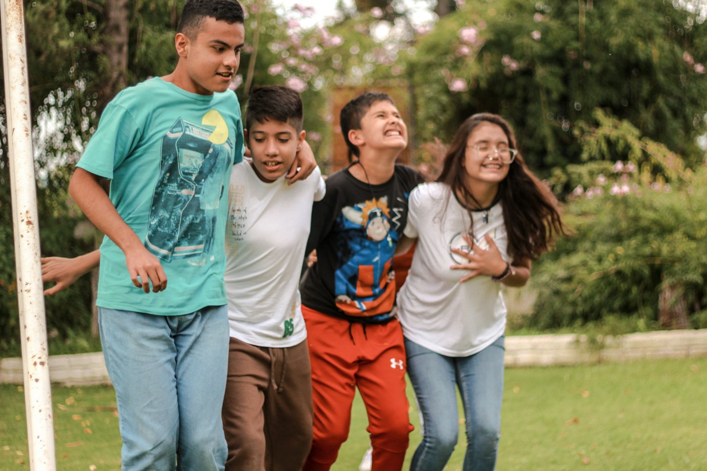 Four teens walk arm in arm across a park lawn, laughing together